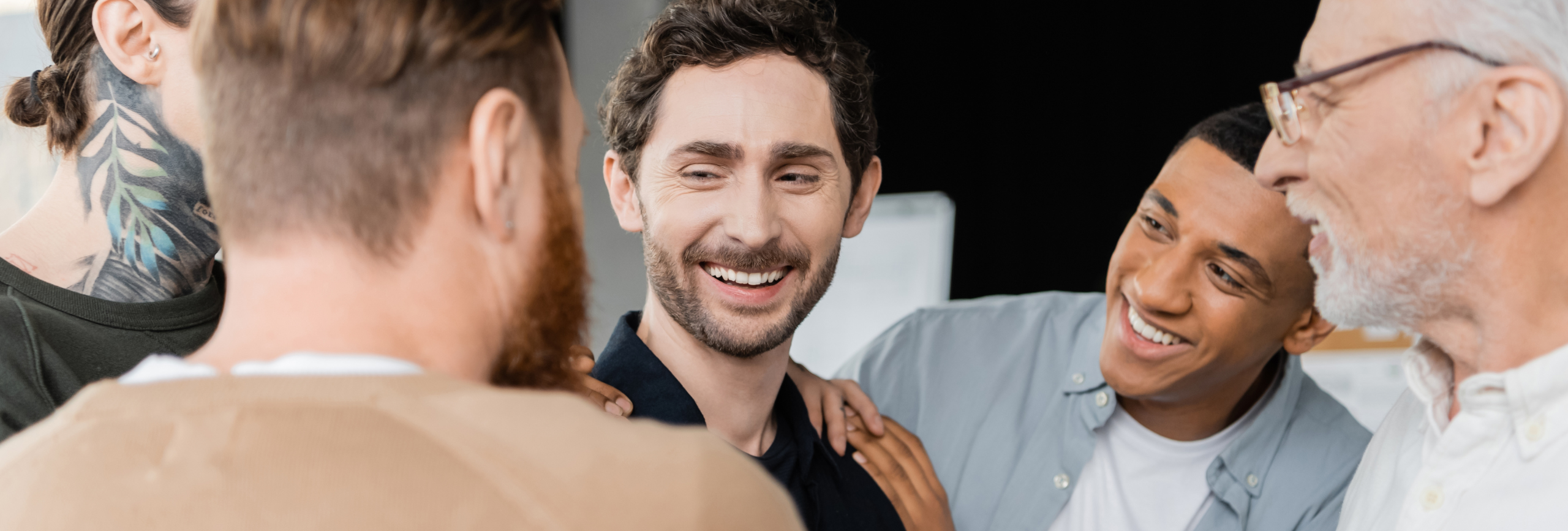 A group of five men stand close together, smiling and talking. One man with a beard is seen from behind, while the others face each other, appearing happy and engaged in conversation—perhaps after a dbt therapy Chicago session.