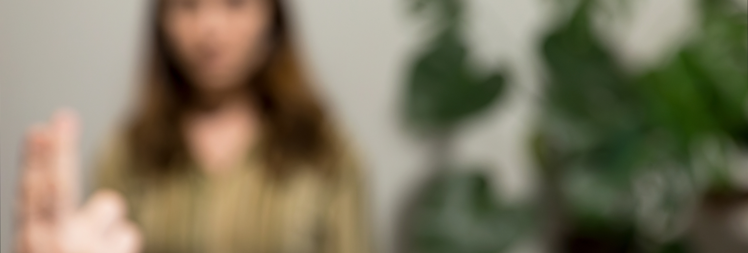 A blurry image showing an indistinct person with long hair in the background and a hand with outstretched fingers in the foreground; large green plants are visible on the right side, evoking a calming space for EMDR Therapy in Chicago.